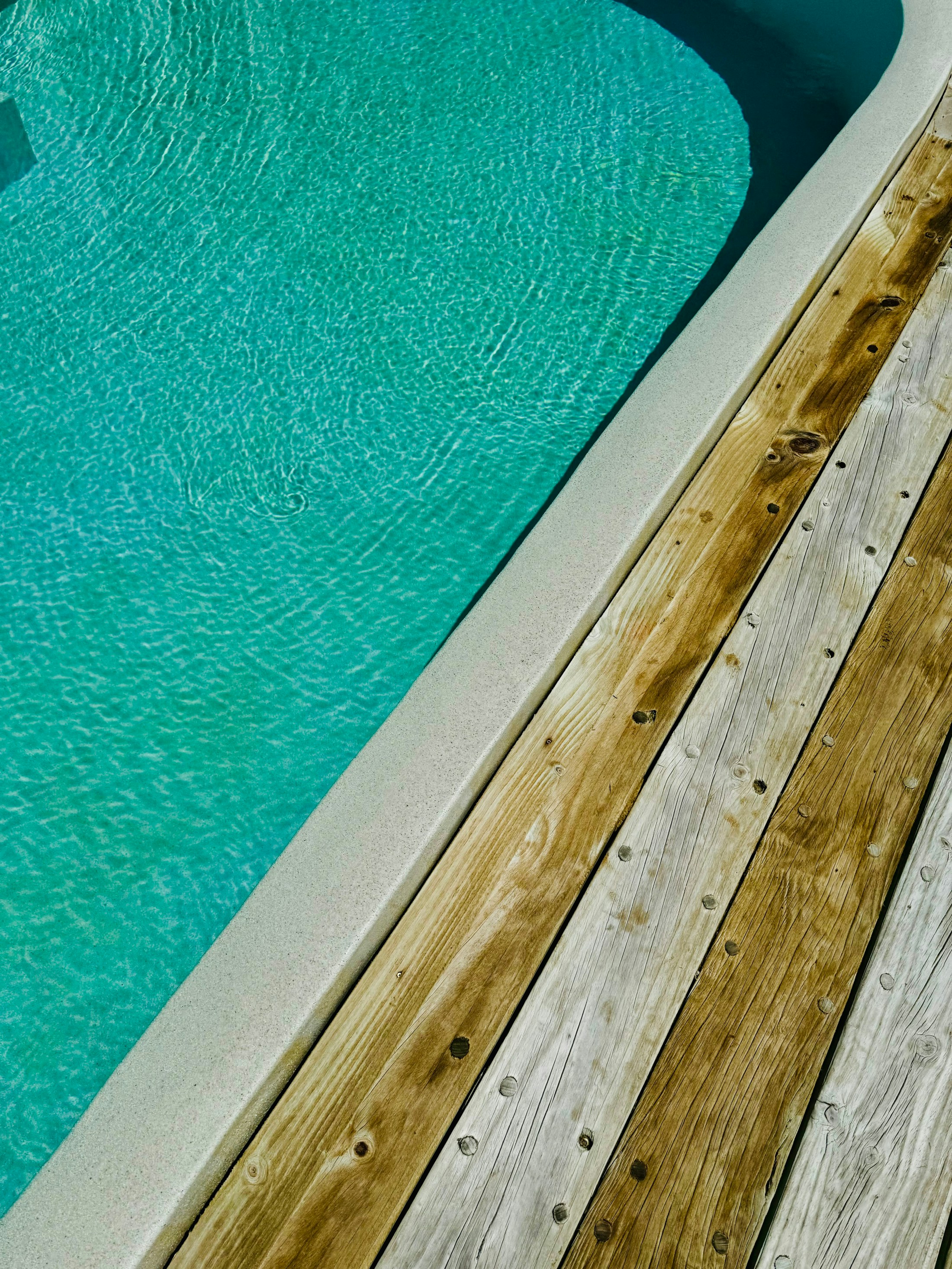 Sunlit blue pool water beside a natural wood deck